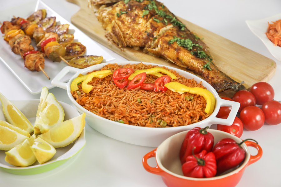 A plated Nigerian meal of jollof rice, grilled fish, and suya skewers